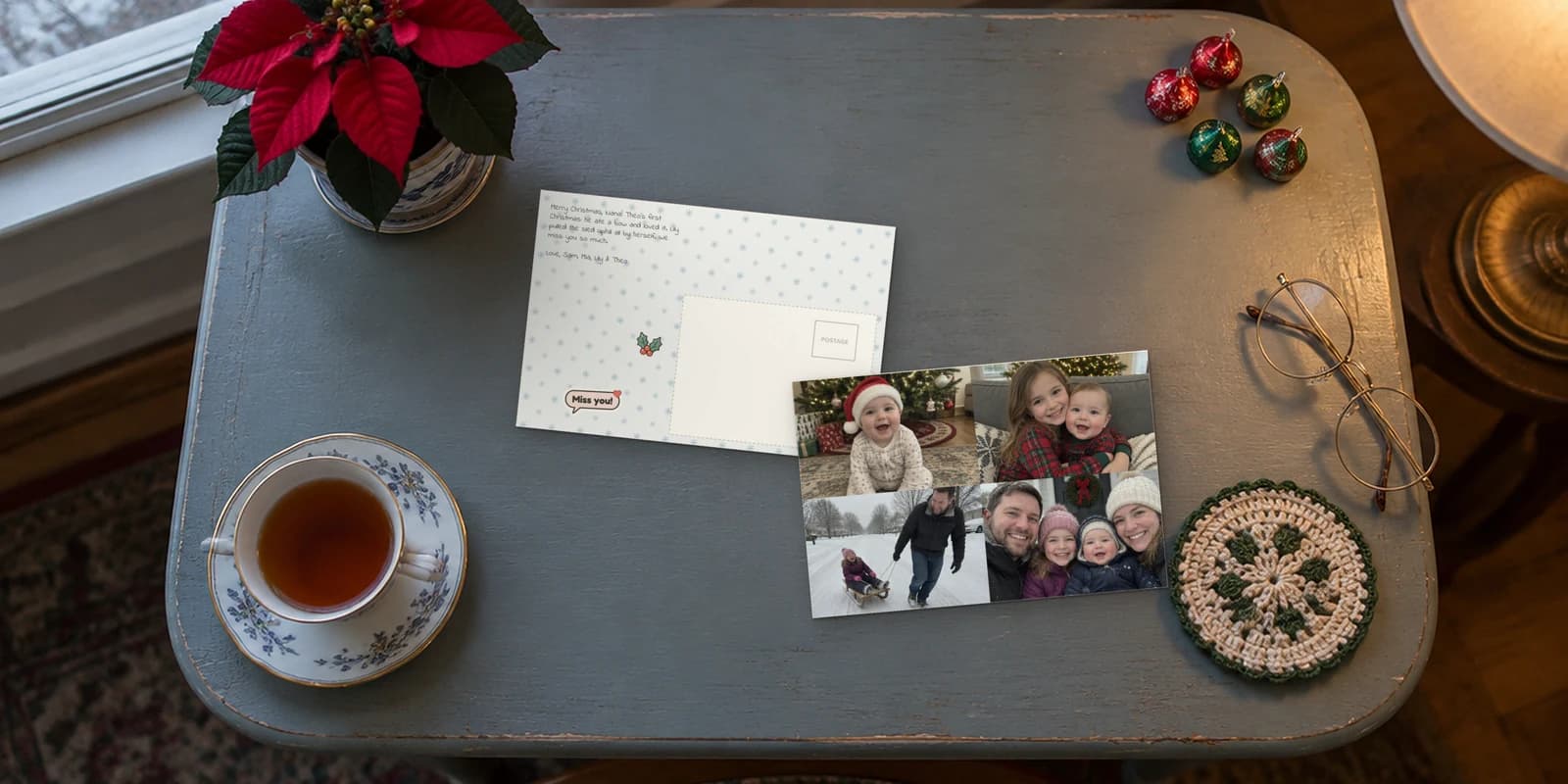 Christmas cards mailed for you: a baby's-first-Christmas photo postcard on a grandmother's side table, beside its snowflake back with a Miss you! sticker
