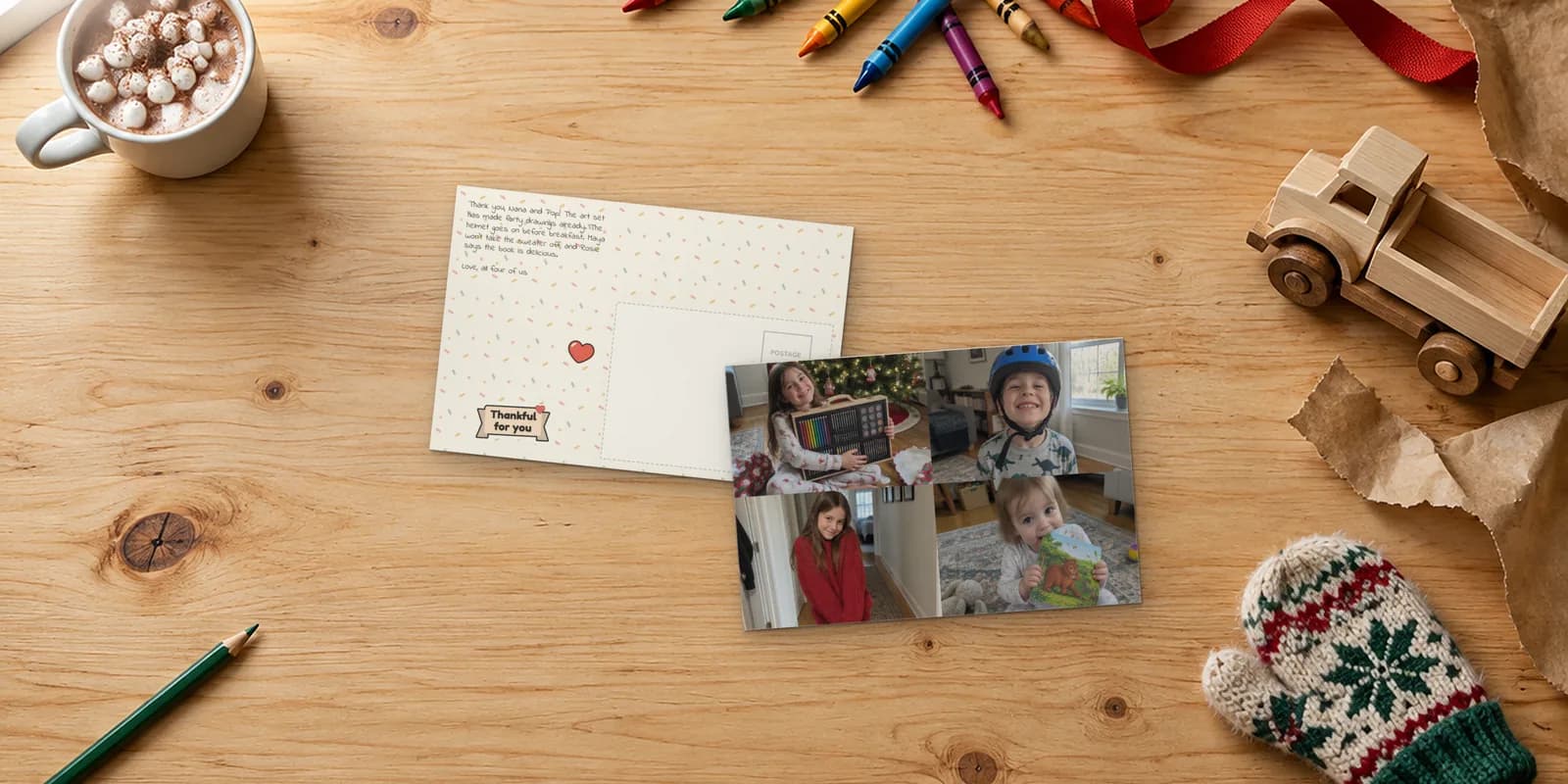 Thank you postcards on a pine kitchen table: a four-photo card of kids with an art set, a bike helmet, a red sweater and a picture book, beside its confetti back with a Thankful for you banner