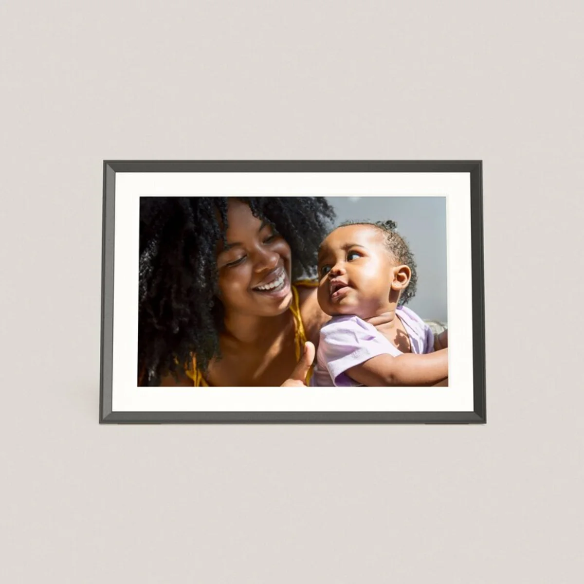 A matted ten-inch digital photo frame on a wall showing a mother laughing with her baby