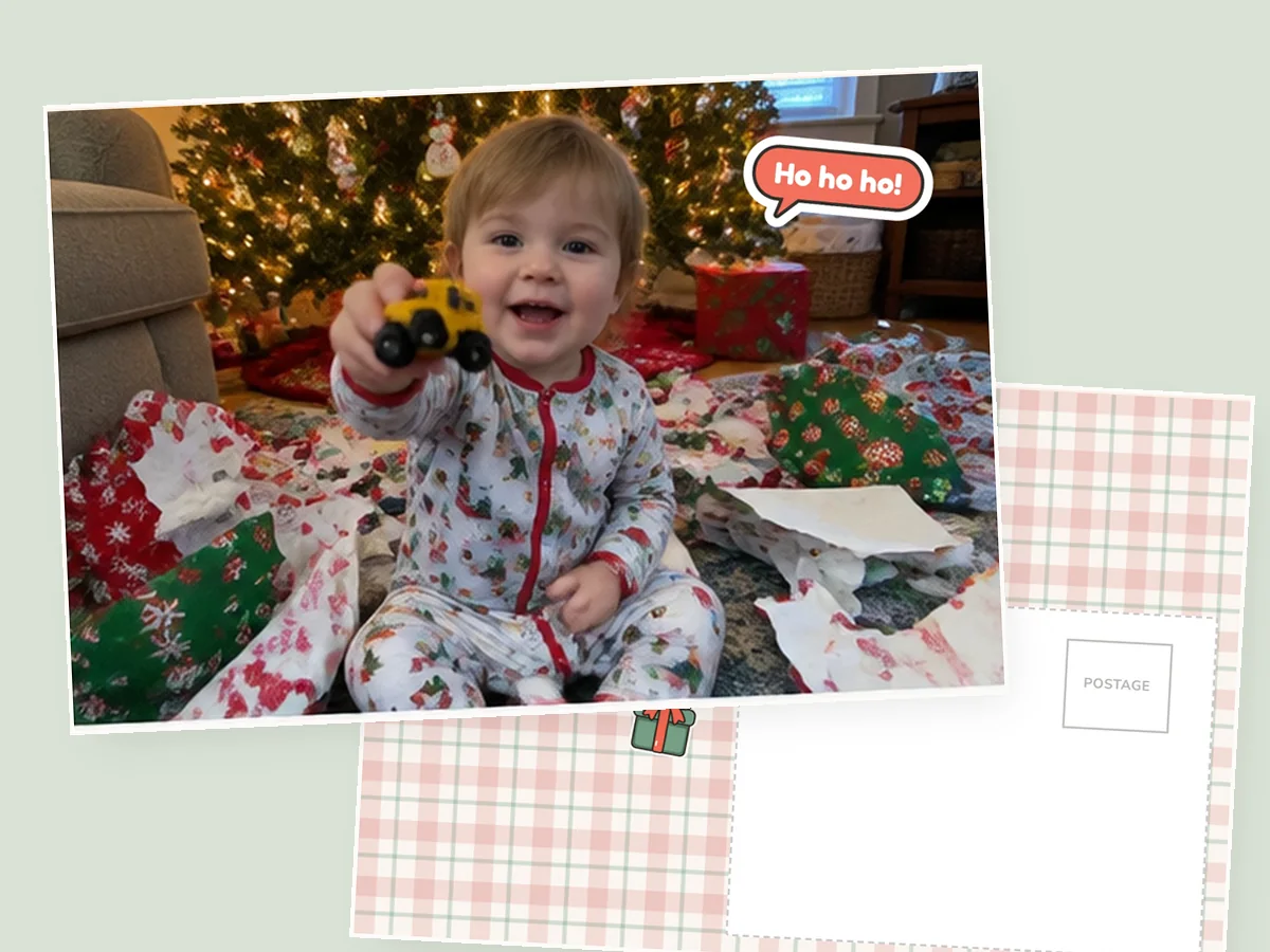 A printed 4×6 postcard of a toddler sitting in a pile of wrapping paper, with a Ho ho ho sticker, its plaid message side underneath