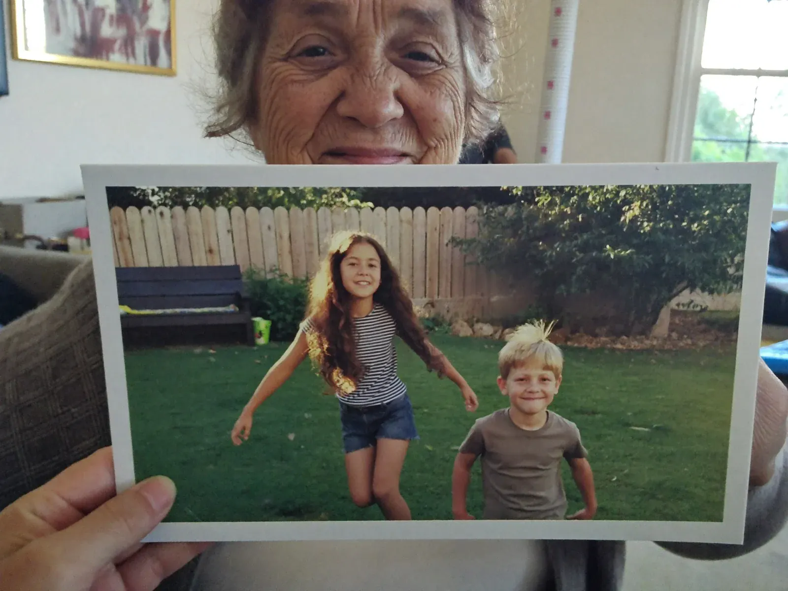 A grandmother smiling as she holds up a printed postcard showing a photo of her grandchildren
