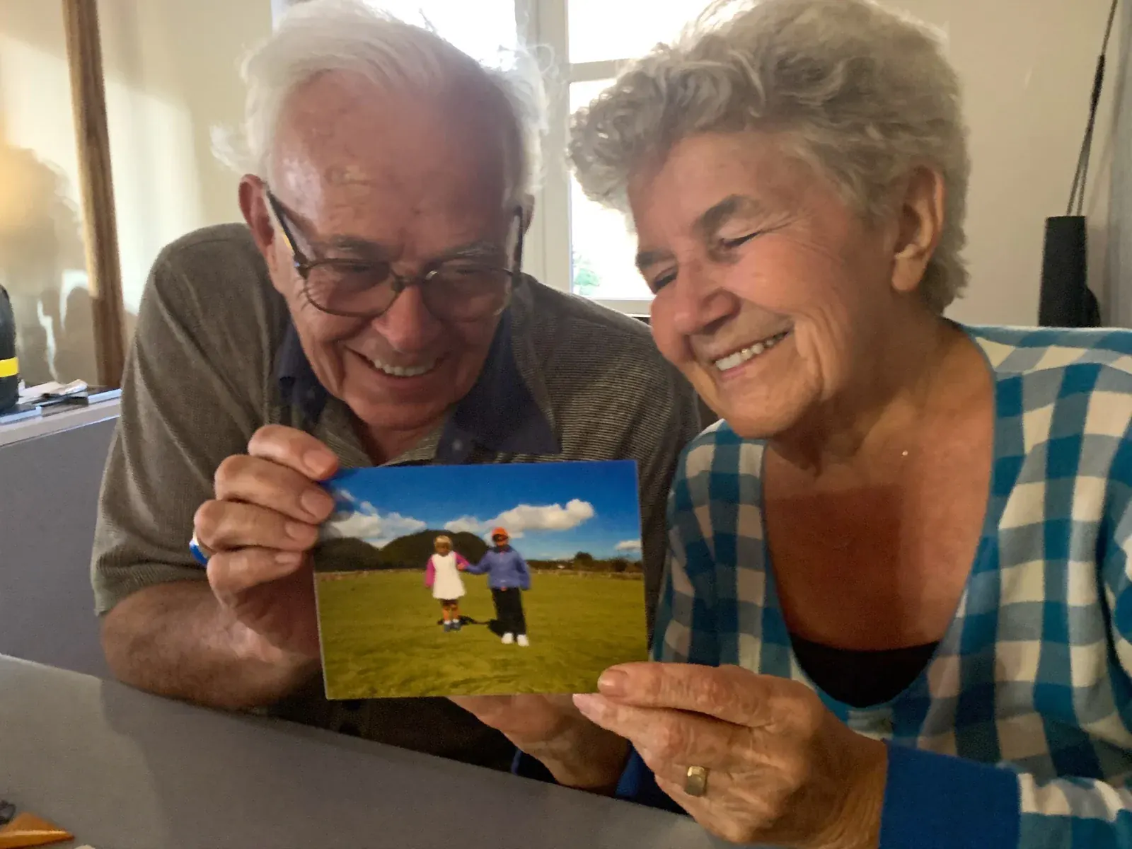 Two smiling grandparents at their kitchen table looking at a FamilyLetter postcard, one of the monthly gifts for grandparents that arrives by mail