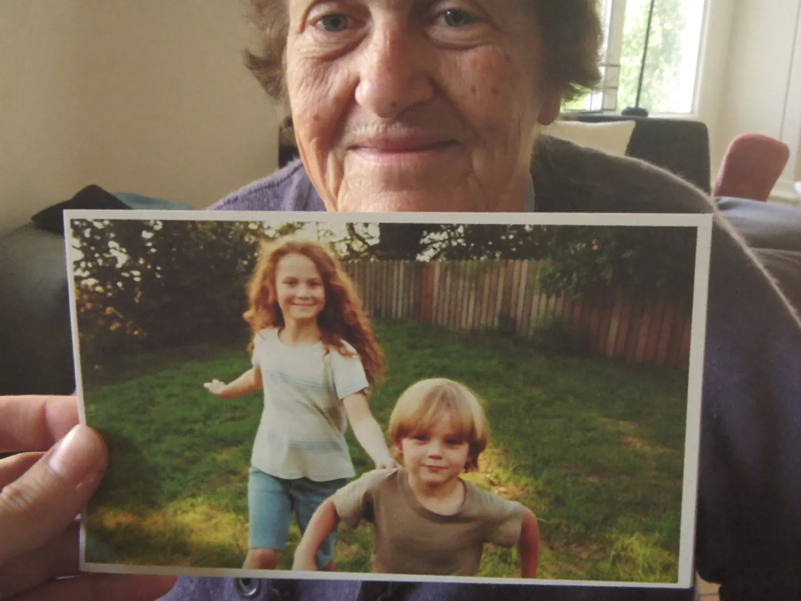 A grandmother smiling as she holds a postcard printed with a photo of her grandchildren