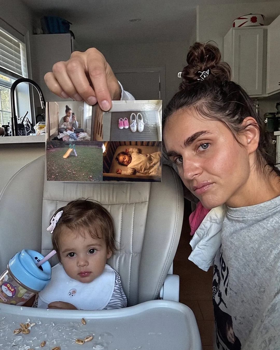A mom in the kitchen holding up a photo postcard next to her baby in a high chair