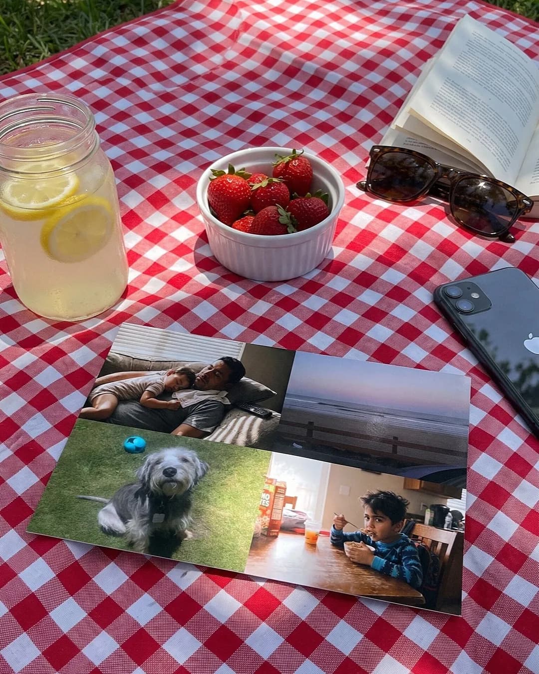 A photo postcard on a red gingham picnic blanket with lemonade and strawberries