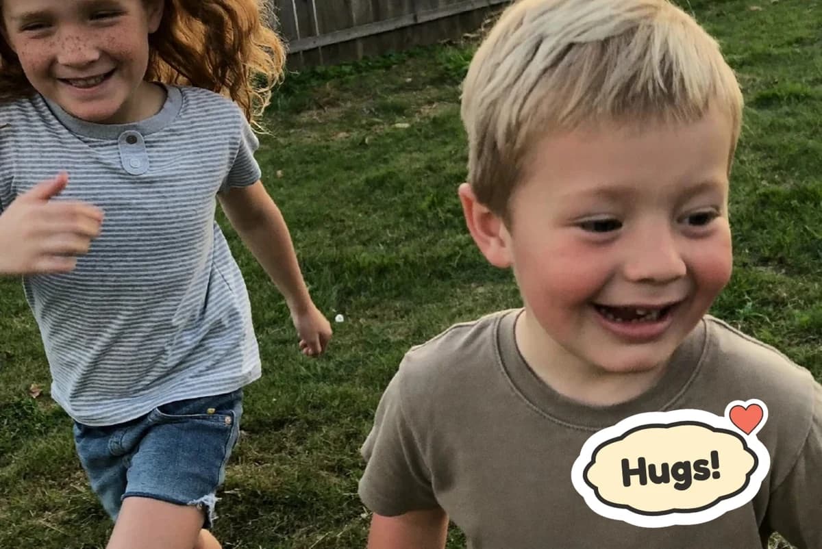 Card front with one photo of a red-haired girl and a laughing blond boy running across a backyard lawn, with a Hugs sticker