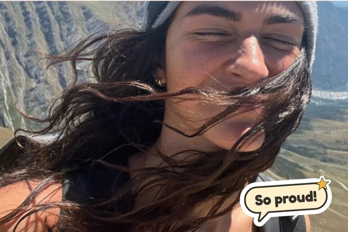 Card front with one full-size photo of a young woman's windblown selfie on a mountain, with a So proud! sticker