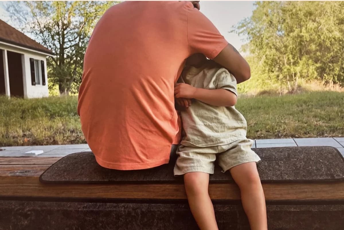 Card front with one photo of a man in a coral T-shirt hugging a small boy on a garden bench