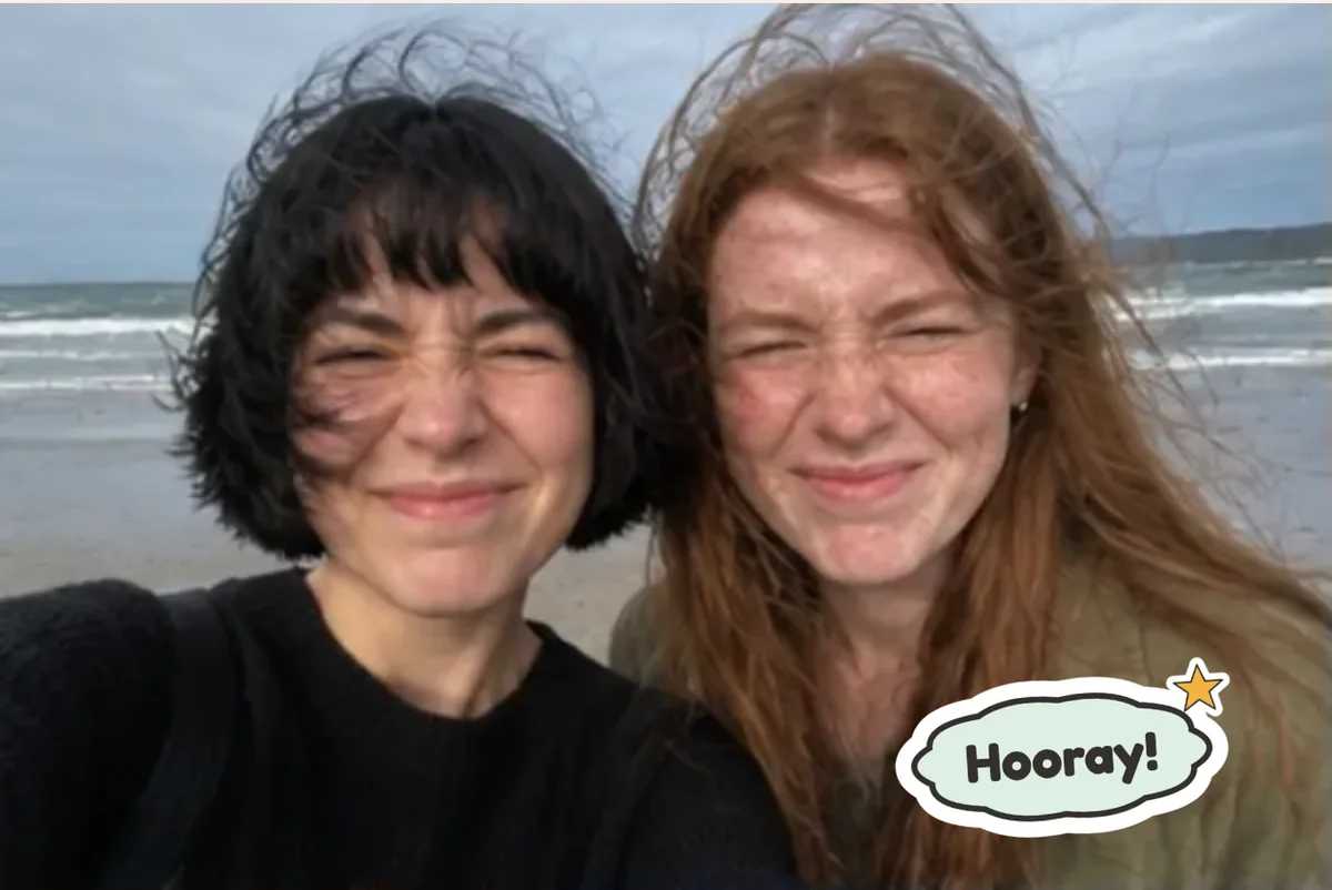Card front with one photo of two young women laughing on a windy beach, with a Hooray! sticker