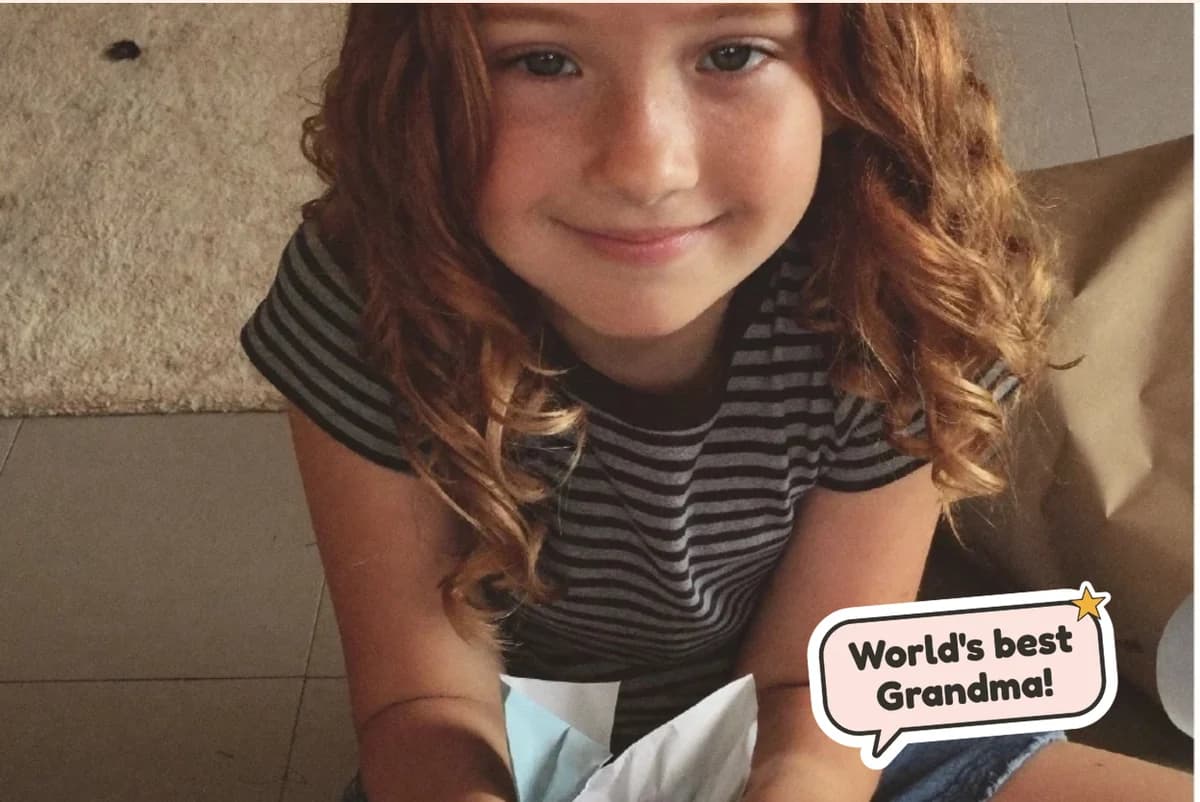 Card front with one full-size photo of a smiling girl with red curls opening a package, with a World's best Grandma! sticker