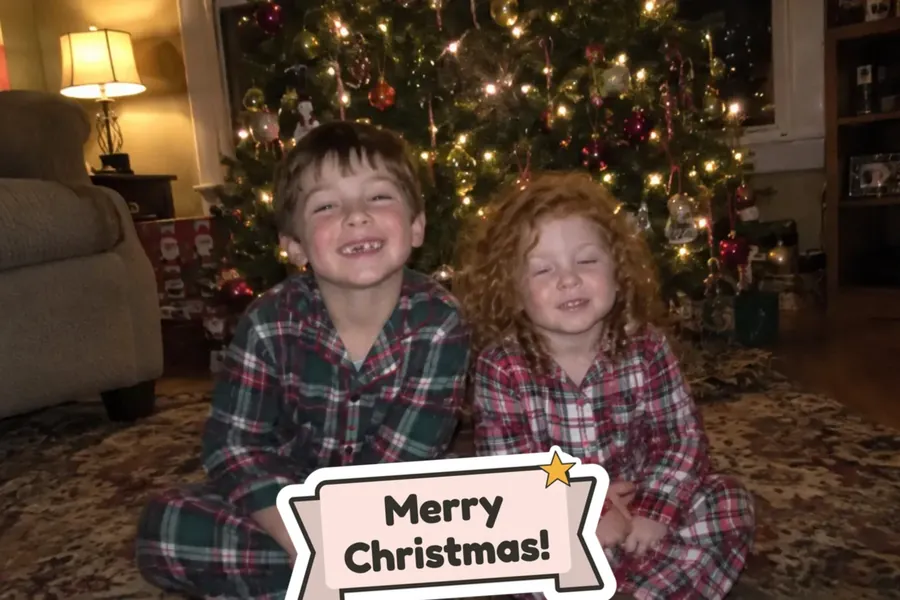 Single-photo Christmas card front: two kids by the tree with a Merry Christmas sticker